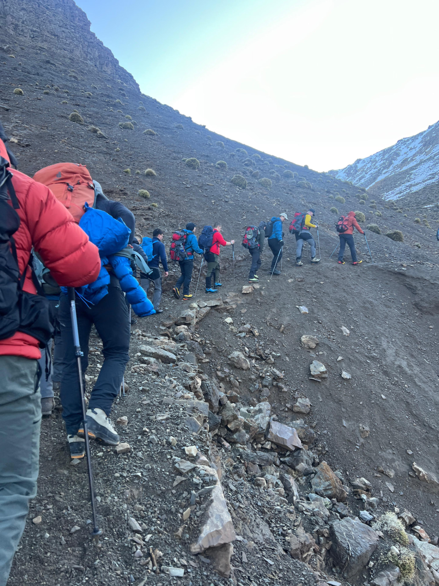 Trekkers ascending a steep rocky, snow-dusted slope in the M’Goun massif, Central High Atlas, Morocco